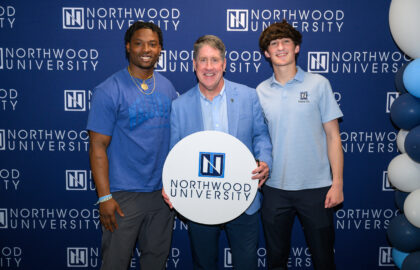 Two honors students pictured with President Kent MacDonald. Northwood University backdrop and balloons while Kent holds a white circle sign with the Northwood University logo.