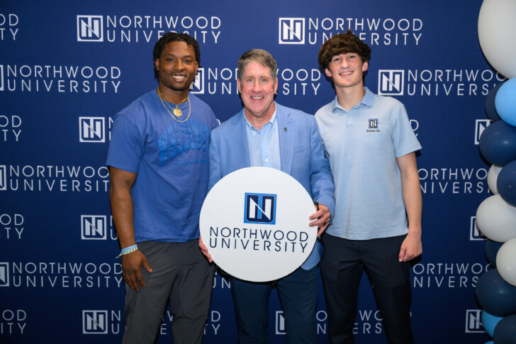 Two honors students pictured with President Kent MacDonald. Northwood University backdrop and balloons while Kent holds a white circle sign with the Northwood University logo.