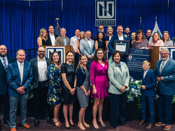 A group of people dressed in formal attire pose together on a stage in front of a Northwood University backdrop, proudly holding certificates and plaques from Northwood's Outstanding Alumni Awards.